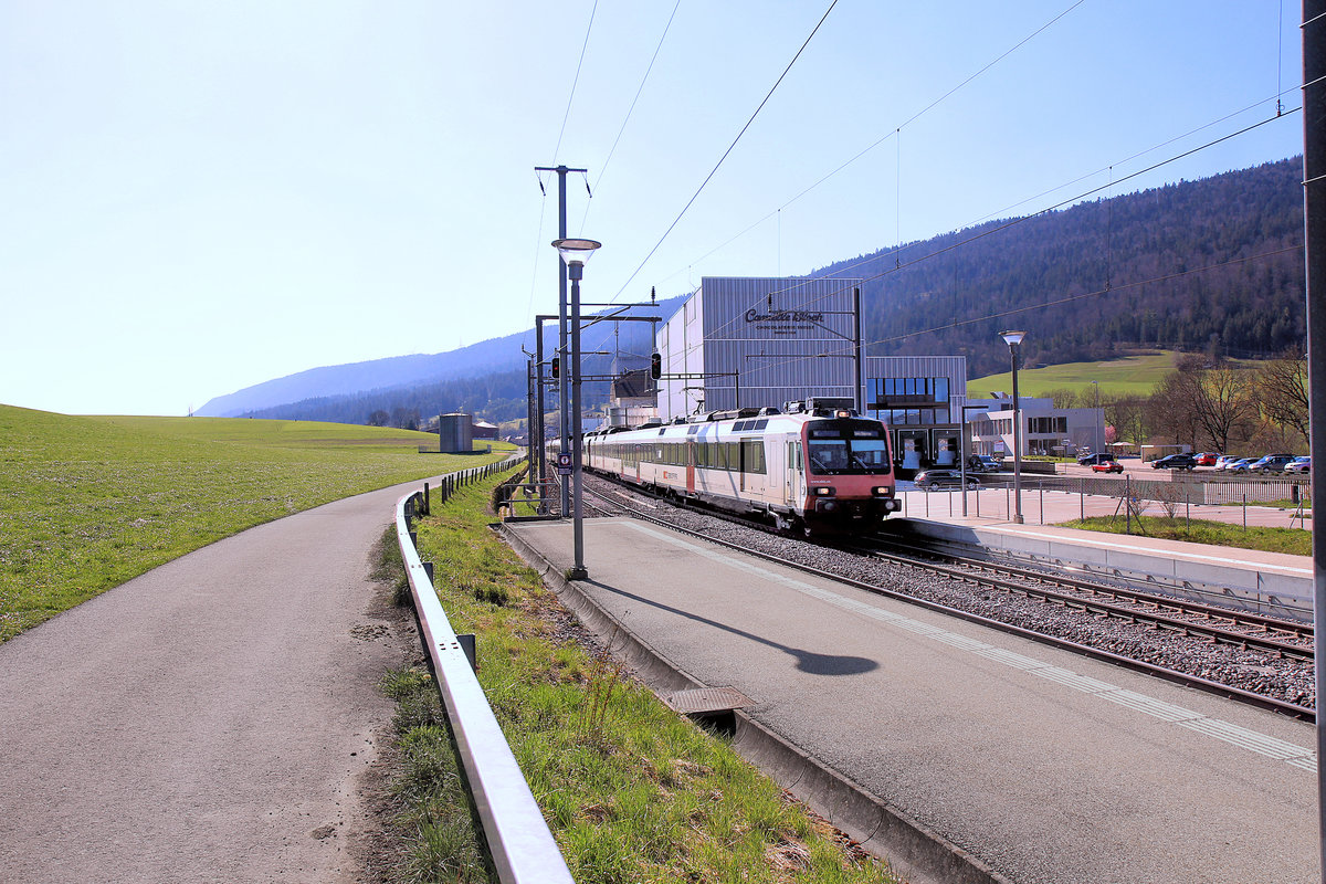 Abendsonne in Courtelary. Zwei zusammengekuppelte NPZ Domino (mit Triebwagen 560 223 und 560 230) fahren von La Chaux-de-Fonds ein. Dahinter das Wahrzeichen von Courtelary, die berühmte Schokoladenfabrik von Camille Bloch. 23.April 2021 