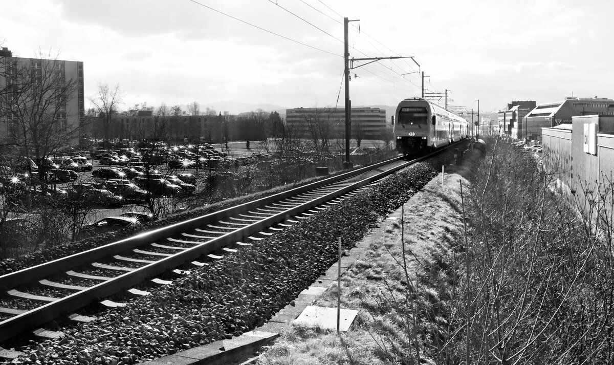 Auf der Zürcher S7 über Kloten: Einfahrt einer S7, von Rapperswil kommend, in Kloten-Balsberg. Praktisch jedes Auto im grossen Parkplatz funkelt wie ein Stern. 6.Februar 2023  