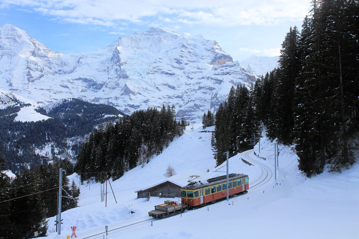 Bergbahn Lauterbrunnen - Mürren: Triebwagen 23 nähert sich von Mürren kommend Grütschalp. Hier wird der auf dem vorausfahrenden Güterwagen geladene Behälter auf das Traggerüst unterhalb der Luftseilbahnkabine gesetzt und nach Lauterbrunnen hinunter transportiert. 14. Dezember 2020 