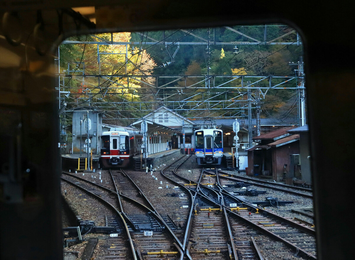 Der Nankai-Konzern, Partnerbahn der MOB:  Nankai  steht für  Süden  und  Meer  und verweist auf eine alte Handelsstrasse von Osaka der Küste entlang zur Stadt Wakayama und weiter nach Süden. Der Nankai-Konzern besitzt 154,8 km Bahnlinien (1067 mm Spur), bestehend aus zwei Hauptlinien von Osaka aus (einschliesslich eines Zweigs zum Internationalen Flughafen Kansai) und einem ganzen Bündel von kurzen Stichlinien. Im Mittelpunkt der am 24.Oktober 2017 geschlossenen Partnerschaft mit der MOB steht die rund 64 km lange Strecke von Osaka zum Berg Kôya (Kôya-san). Kôya-san ist eine auf knapp 900 Metern gelegene, aus dem 9.Jahrhundert stammende Tempelstadt mit zahlreichen Gebäuden, die zum Unesco-Weltkulturerbe gehören. Die Bahn erreichte Kôya-san im Jahre 1930; genau genommen endet die Adhäsionsstrecke (mit 50 Promille Steigung) im dicht bewaldeten Gokuraku-bashi ( Brücke zum Paradies , 538 m.ü.M.). Von da führt eine Standseilbahn auf 863 m.ü.M., wo ein Bus den Anschluss ins Städtchen Kôya-san herstellt. Im Bild ein Blick aus einem ausfahrenden Zug auf zwei wartende Züge im Bahnhof Gokuraku-bashi, links ein Express direkt in die Stadt Osaka (Zug 31001), rechts ein Lokalzug, der ins Tal hinunter nur bis Hashimoto pendelt (Zug 2037). Ganz rechts die Verbindungsgalerie zur Standseilbahn. 5.November 2022    