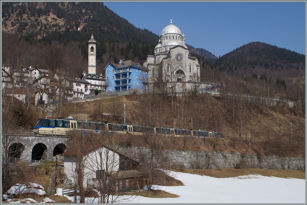 Der SSIF Treno Panoramico Vision Vigezzo vor der Kulise der Wahlfahrtskirche  Madonna del Sangue  in Re. Zwischen von hier einige hundert Meter westliche gelegenen Bahnhof Re und dem  in der Schweiz liegenden Camedo verkehren bis auf wenige Ausnahmen nur die internationalen Züge, das der Regionalverkehr von Domodossola und Locarno in den vorgenannten Stationen endet. 
19. März 2015