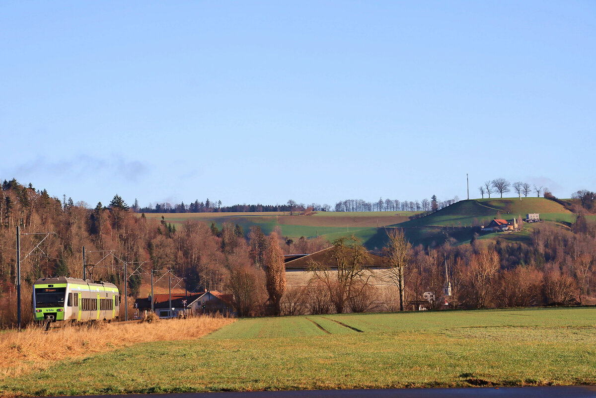 Die ehemalige VHB (Vereinigte Huttwil-Bahnen) / Strecke der ursprünglichen Huttwil-Wolhusen Bahn (HWB): BLS NINA 525 028 hat Hüswil Richtung Osten (und dann Süden) verlassen und wird bald im luzernischen Zell halten, dessen hoher Kirchturm im Hintergrund sichtbar ist. 31.Dezember 2021 