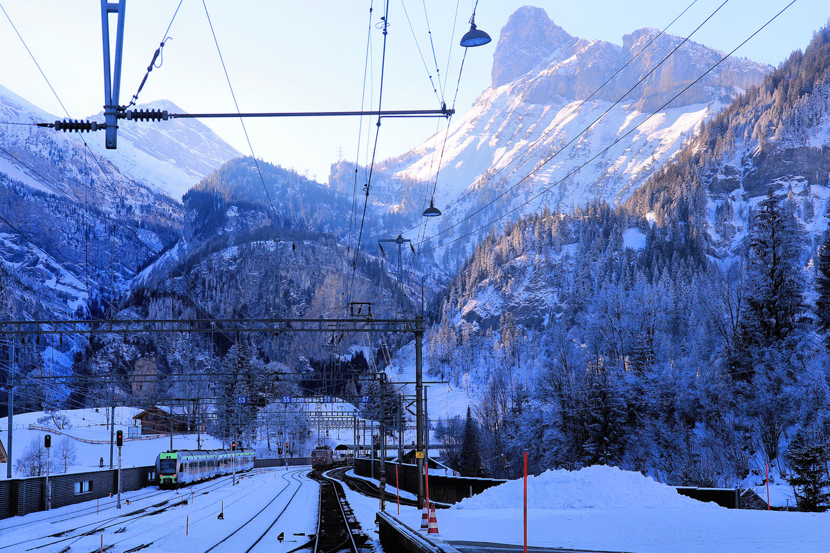 Die Züge wirken ganz winzig in der überwältigenden Berglandschaft von Kandersteg. Links die BLS Lötschberger-Züge 118 und 111 (der vordere Zug nach Domodossola), und rechts fährt gerade ein Autozug von Goppenstein mit BLS Lok 195 ein. 