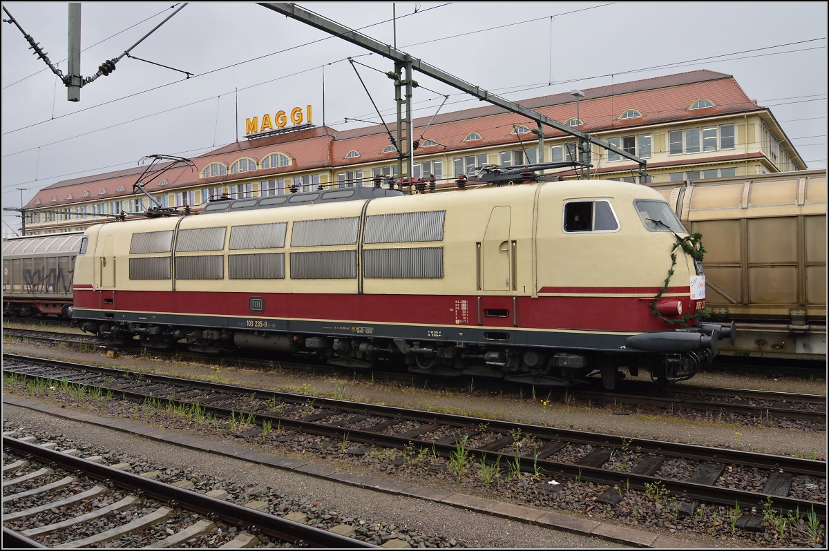 Ein Besuch in Singen am Hohentwiel. Man glaubt es kaum, aber 103 235-8 kommt zur letzten Fahrt eines Tf ausnahmsweise nach Singen. Der Klassiker mit der Maggi im Hintergrund, leider ein wenig zugestellt. April 2014.