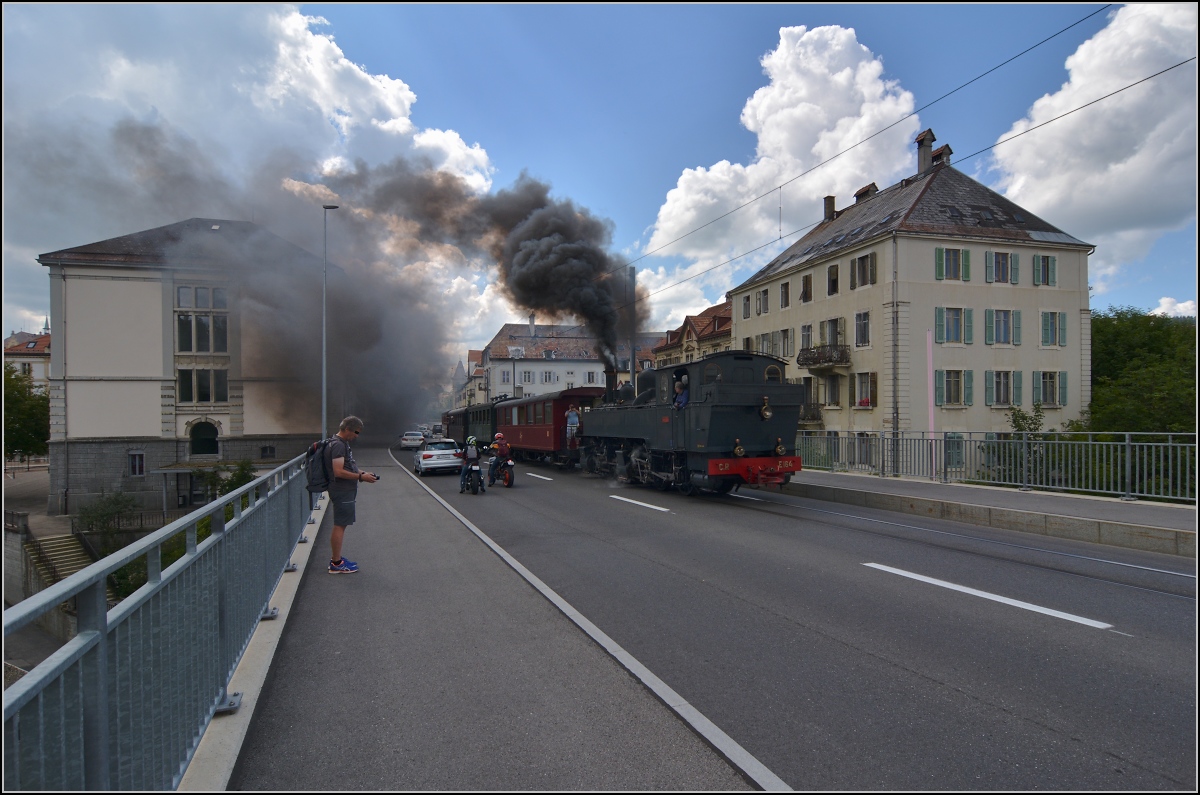 Eine etwas ungewöhnliche Verkehrsteilnehmerin in La Chaux-de Fonds. 

Rette sich, wer kann. Denn CP E 164, heute bei La Traction, schnaubt mit viel Rauch als Geisterfahrerin die Rue du Manège hinauf. So sammeln sich respektvoll immer mehr Autofahrer und Motorradfahrer auf der falschen Strassenseite. Den Blick auf das Weltkulturerbe kann sie aber nicht ganz verstellen. September 2021.