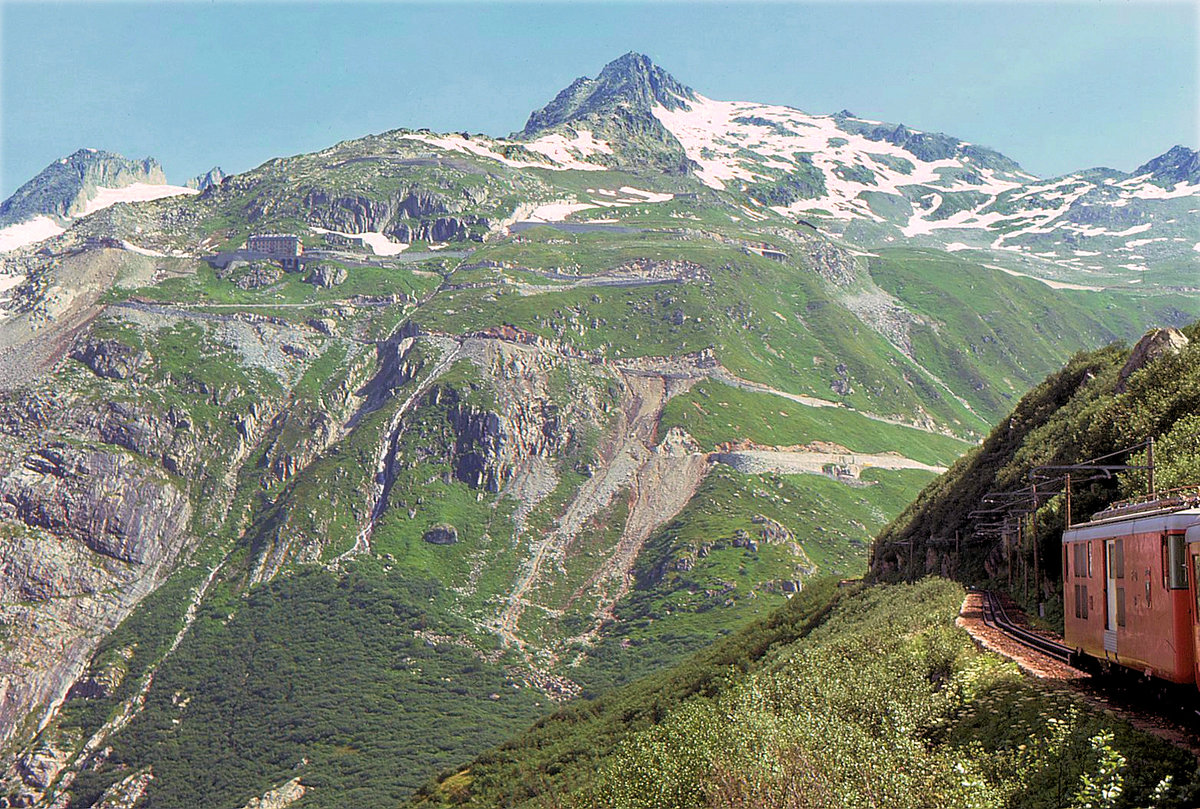 Furka Bergstrecke zur Zeit des elektrischen Betriebs: FO Triebwagen 53 zieht ihren Zug von Gletsch zum Furka-Tunnel hinauf, mit Blick auf die Furka Passstrasse. 28.Juli 1975 
