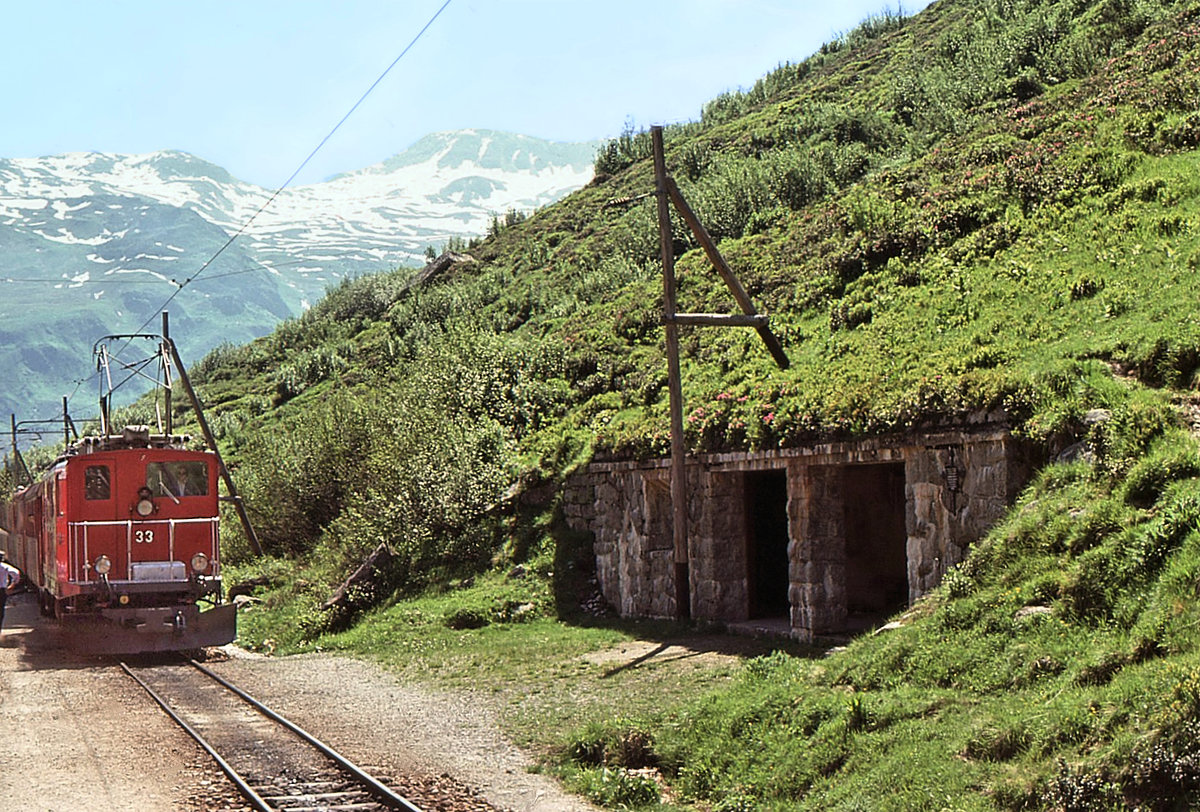 Furka Bergstrecke zur Zeit des elektrischen Betriebs: Kreuzung in Tiefenbach mit einem Zug Richtung Brig, geführt von FO HGe4/4 33. 28.Juli 1975 