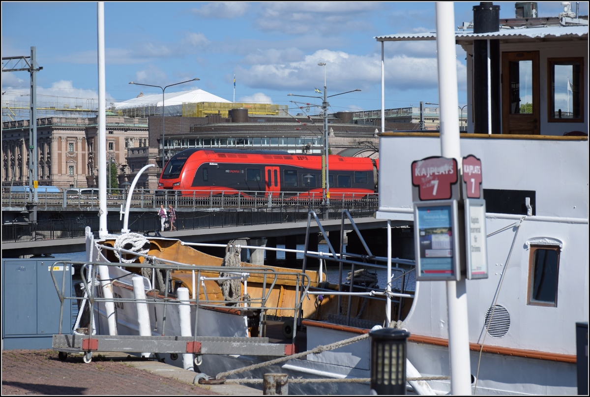 Hochgeschwindigkeits-Flirt in Schweden. 

X74 003 'Rödluvan' schiebt sich zwischen den Königspalast und die Mariefred, eines der unzähligen Dampfschiffe in Stockholm. Juni 2018.