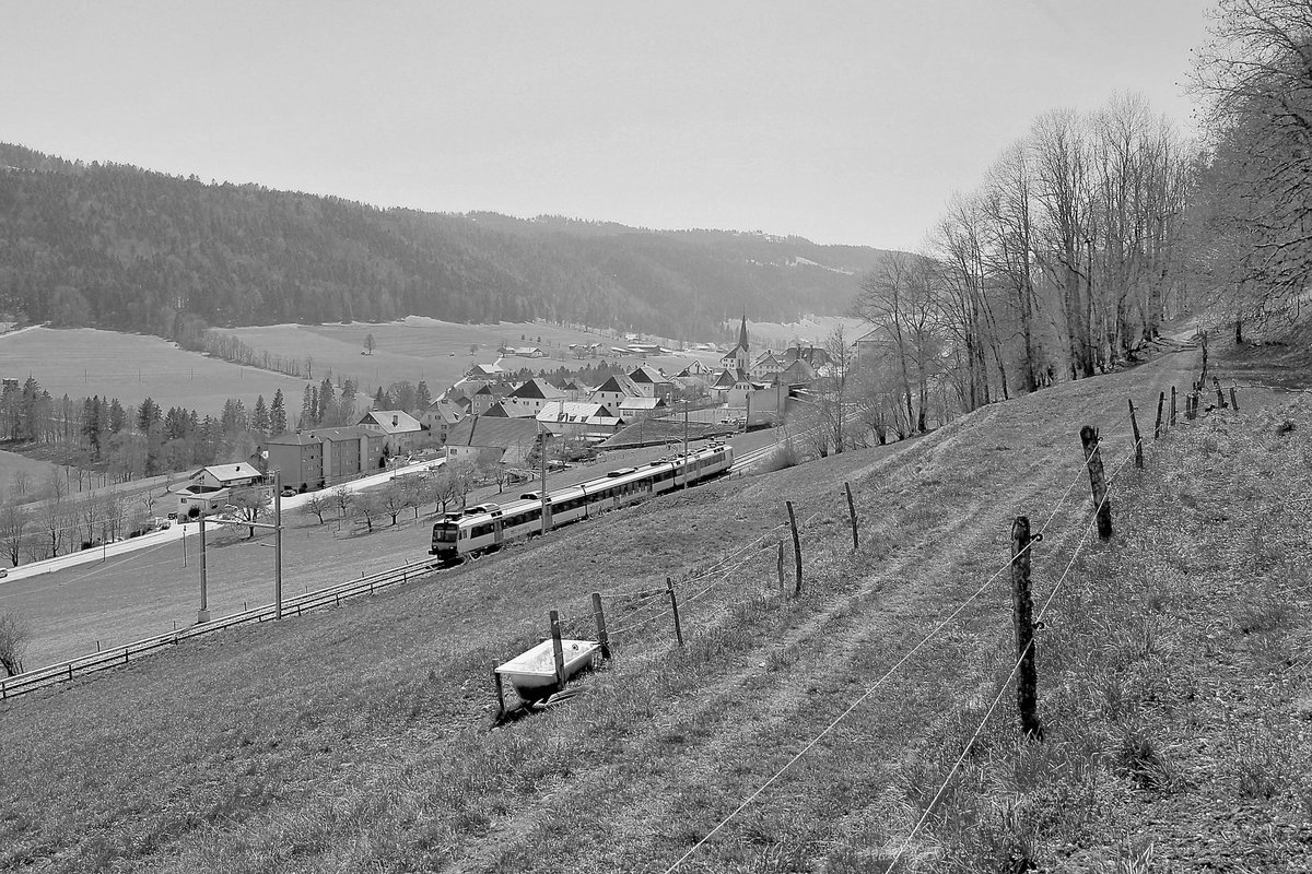 Renan (Kanton Bern). Ausfahrt eines NPZ Domino-Zugs aus dem obersten Städtchen im Tal mit seinen markanten kubischen Häusern, Mietshäuser aus dem 19.Jahrhundert, als die Uhrenindustrie hier zentral wurde. 23.April 2021 