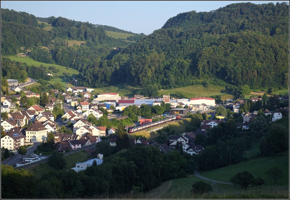 Umleiterverkehr auf dem Läufelfingerli. Ein IC hat in Läufelfingen gerade den Hauensteintunnel verlassen, rechts kann man gerade noch den Tunneleingang erkennen. Da die alte Bergstrecke namensgleich mit der Basislinie ist, wurde die Gemeinde Läufelfingen im Bild der neue Namensgeber, obwohl die Strecke eigentlich als zweitälteste Bahnlinie der Schweiz ist den Vorrang haben sollte... ;-) Im Hintergrund ist deutlich der Mittelgebirgscharakter des Jura zu erkennen, der den Bau der Strecke erschwerte. So dauerte es 4 Jahre vom ersten Zug 1854 bis zur vollständigen Eröffnung, leider wurden bei einem Brand während des Tunnelbaus 63 Menschen durch Kohlenmonoxid vergiftet. Juli 2018.