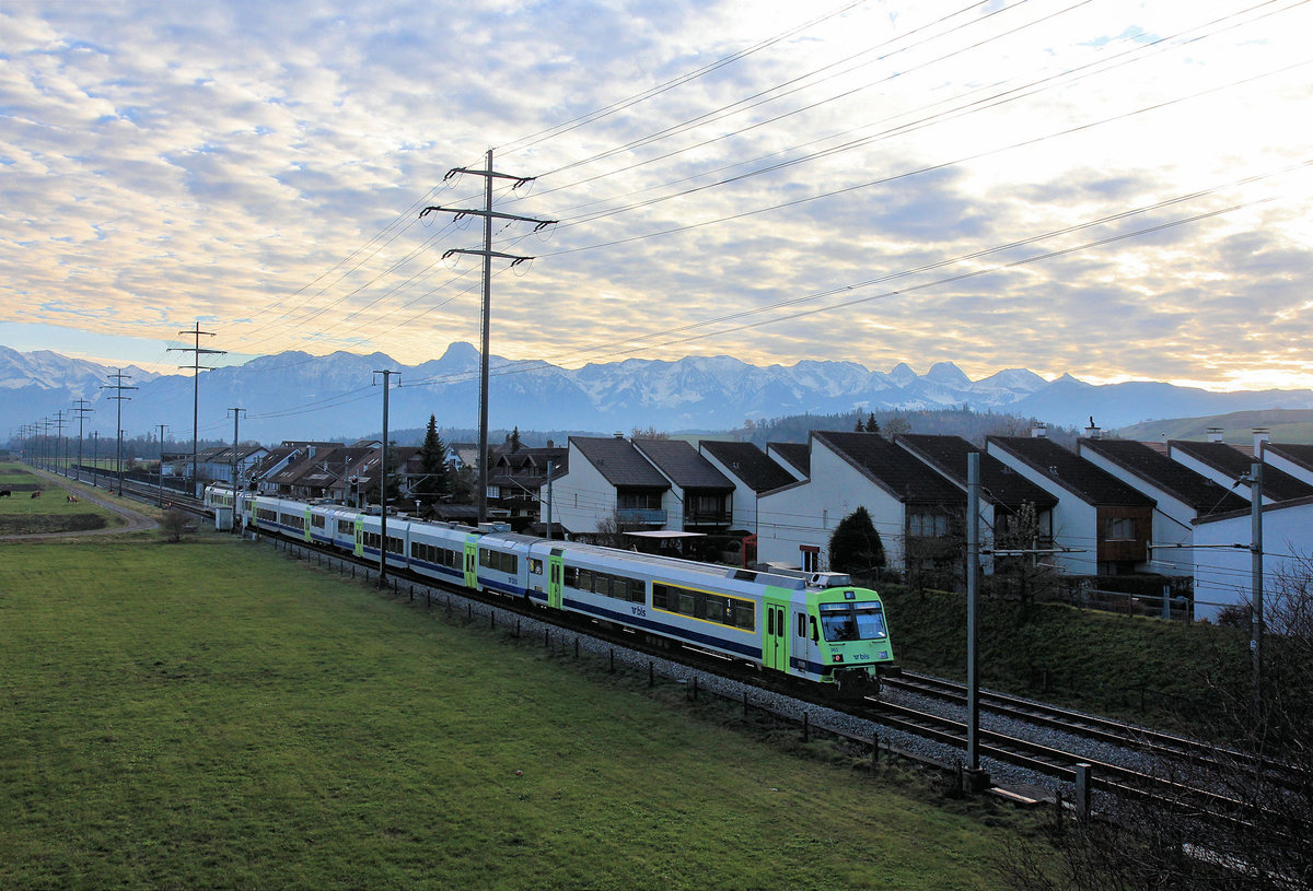 Zugsvielfalt bei Sonnenuntergang an der Bahnstrecke Bern-Thun: Ein NPZ der BLS, hier auf Dienstfahrt ohne Fahrgäste. Dem klopfenden Geräusch nach hatte er eine schwere Flachstelle. Angeführt von NPZ Triebwagen 725, zuhinterst Steuerwagen ABt 965. Wichtrach, 23.Nov.2020 