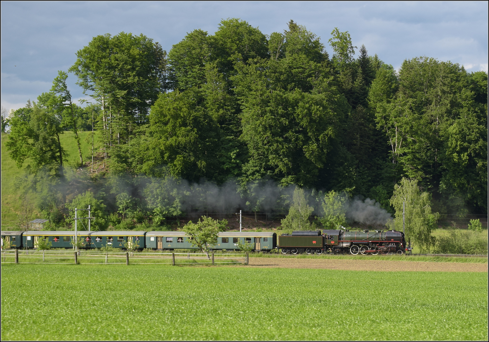 150 Jahre Emmentalbahn. 

141-R-1244 auf dem R�ckweg von der grossen Emmentalrundfahrt anl�sslich des Jubil�ums. Am Ortsausgang Menznau findet die Sonne ein Wolkenloch, freie Sicht auf die Strecke und die Strasse ist ohne Verkehr. Menznau Tuetisee, Mai 2025.