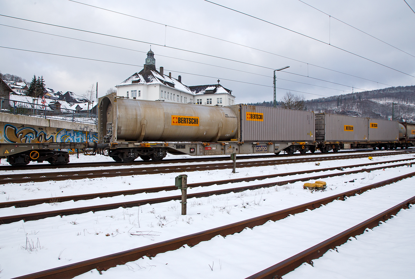 4-achsiger Drehgestell-Containertragwagen 31 85 455 218-3 CH-SBBC, der Gattung Sgnss (60ft), der SBB Cargo AG, im Zugverband am 21.01.2023 bei der Zugdurchfahrt in Niederschelden (Sieg), beladen mit einem 30´ Tank-Containern und einem 30´ ISO-Containern von dem Logistikdienstleister Bertschi AG (Dürrenäsch/Schweiz).

TECHNISCHE DATEN:
Spurweite: 1.435 mm
Anzahl der Achsen: 4 in zwei Drehgestellen
Länge über Puffer: 19.990 mm
Drehzapfenabstand: 14.420 mm
Achsabstand im Drehgestell: 1.800mm
Laufraddurchmesser: 920 mm (neu)
Ladelänge : 18.720 mm  (60 ft)
Höhe der Ladeebene über SOK: 1.155 mm
Höchstgeschwindigkeit: 100 km/h Lastgrenze S / 120 km/h bei Lastgrenze SS und leer)
Max. Zuladung bei Lastgrenze S: 70,0 t (ab Streckenklasse D)
Max. Zuladung bei Lastgrenze SS: 60,0 t (ab Streckenklasse C)
Eigengewicht: 20.000 kg
Kleinster bef. Gleisbogenradius: R 75 m
Bauart der Bremse: DK-GP-A (K)
Bremssohle: Cosid 810
Intern. Verwendungsfähigkeit: RIV
Wageneinrichtungen: 36 Umklappbare Aufsetzzapfen
