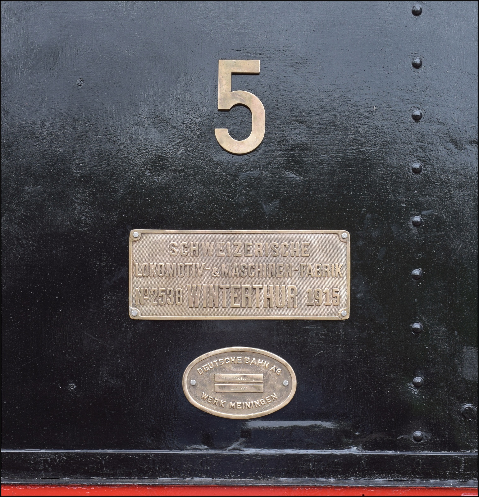 Abstecher zur Coni'fer. 

Ein Blick auf die Fabrikschilder des vor sich hin dampfenden Tigerli E 3/3 5 in Les Hôpitaux-Neufs. Mai 2023.