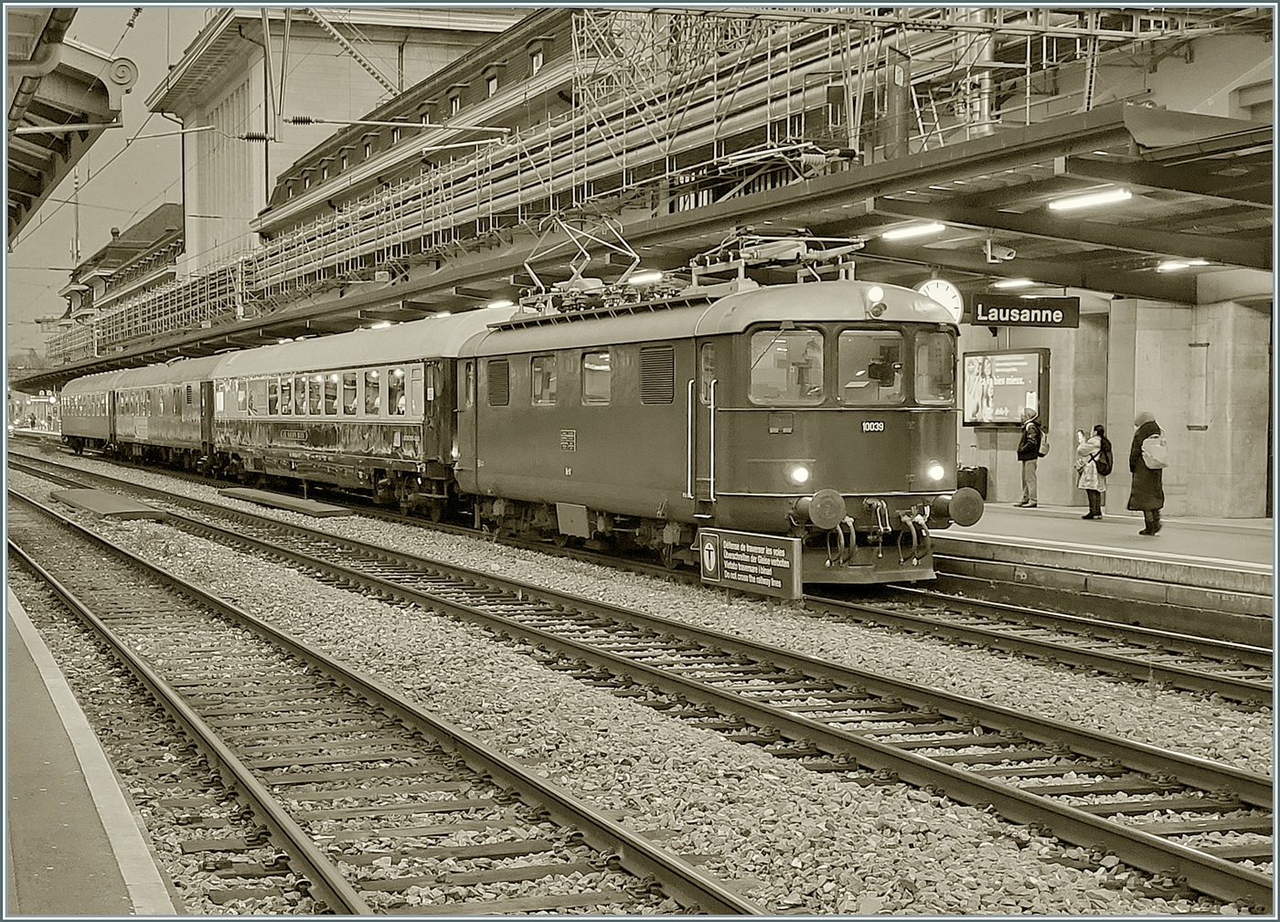 Als S/W Version: Die Re 4/4 I 10039 stellt den Extrazug 31131 in Lausanne bereit. Der Zug verkehrt für eine Reisegruppe nach Zürich Enge (mit Halt in Palézieux). Der Zug besteht aus dem  Le Salon Bleu  61 85 80-90 200-6 CH-IRSI, dem 56 80 89-80 010-2 WGm D-IRSI und dem Am 56 80 10-40 360-4 D-IRSI. Da der TEE Rheingold Genève - Amsterdam am Schluss seiner Einsatzzeit vor vielen Jahren aus einem DB Speisewagen, einem DB Abteilwagen und einen DB Großraumwagen bestand und auch von einer Re 4/4 I gezogen wurde, weckt der heutige Zug doch Erinnerungen an den TEE 6 / 7, der am 23. Mai 1982 zum letzten Mal ab Genève fuhr, (und sich dann noch gut zwei Jahre auf dem Abschnitt Basel - Amsterdam hielt). Leider die Re 4/4 I 10039 etwas ungeschickt vor dem Schild  Überschreiten der Geleise verboten, und leider waren diese Lichtverhältnisse nichts für meine kleine Knipse, so dass ich hier ausnahmsweise ein Handy-Bild zeige. 11. Dezember 2024