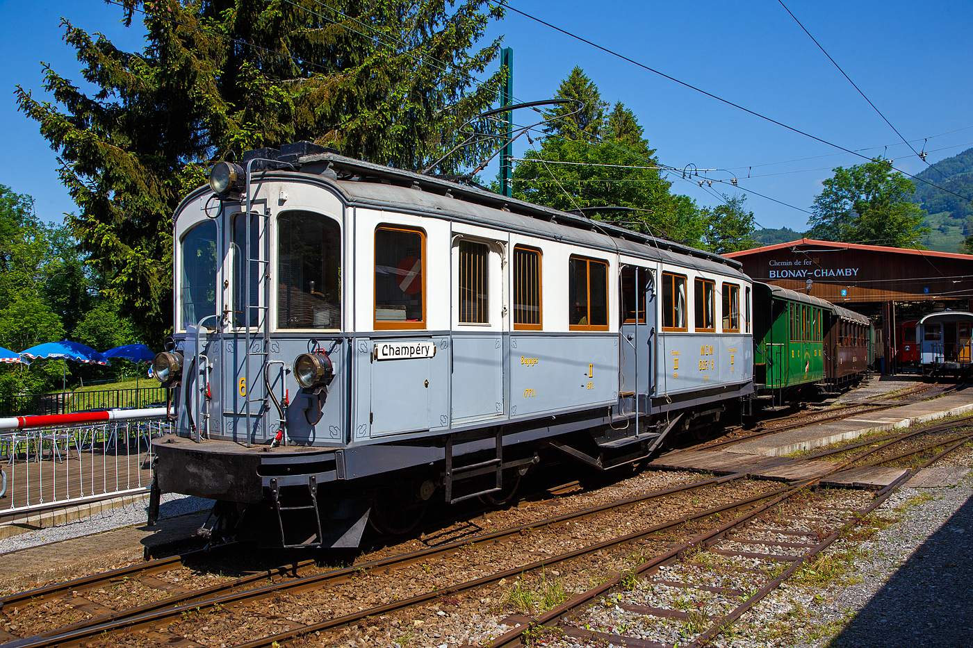Der 2./3. Klasse elektrische Personentriebwagen mit Gepäckabteil für den gemischten Zahnrad- und Adhäsionsbetrieb ex MCM BCFeh 4/4 6 (nach heutiger Bezeichnung eigentlich BCDeh 4/4) der Museumsbahn Blonay–Chamby steht am 27 Mai 2023 im Museum Chaulin mit einem Zug zur Abfahrt bereit..

Die BCFeh 4/4 1–3 sind elektrische Personentriebwagen mit Gepäckabteil für den gemischten Zahnrad- und Adhäsionsbetrieb, die 1908 zur Betriebseröffnung der meterspurigen Monthey-Champéry-Morgins-Bahn (MCM) beschafft wurden. Im Jahr 1946 entstand durch Fusion der MCM und der Aigle–Ollon–Monthey-Bahn (AOM) die Aigle-Ollon-Monthey-Champéry-Bahn (AOMC), die wiederum fusionierte 1999 mit der AL, ASD und BVB zur der heutigen Transports Publics du Chablais (TPC). 

Die Triebwagen der MCM, späteren AOMC hatten das Zahnstangensystem Strub, 2016 wurden auf der Strecke Aigle–Ollon–Monthey–Champéry die Zahnstangenabschnitte erneuert und das bisherige Zahnstangensystem Strub durch das Zahnstangensystem Abt ersetzt. Fahrleitungsspannung wurde auf 1500 Volt erhöht. Seither besitzen die ab Aigle verkehrenden Strecken der TPC das gleiche Zahnstangensystem und die gleiche Spannung. So können die modernen Stadler Beh 2/6 SURF auf allen drei Strecken verkehren.

Bei dem hier gezeigten MCM BCFeh 4/4 6 (später ABFeh 4/4, ab 1966 ABDeh 4/4) handelt es sich um einen 1909, bereits ein Jahr nach der Betriebseröffnung, erfolgten Gelegenheitskauf eines weitgehend baugleichen Triebwagen, der ursprünglich für die Stresa-Mottarone-Bahn (FSM) in Italien bestimmt war. Die für das Zahnstangensystem Strub ausgelegten Triebwagen wurden von der Schweizerischen Industrie-Gesellschaft in Neuhausen am Rheinfall erbaut, wobei die elektrische Ausrüstung von der Elektrizitätsgesellschaft Alioth in Münchenstein und die Drehgestelle einschl. des Zahnradantriebs von der Schweizerischen Lokomotiv- und Maschinenfabrik (SLM) in Winterthur stammen. Der Triebwagen BCFeh 4/4 6 ist als einziger bei der Museumsbahn Blonay–Chamby (BC) in der Westschweiz erhalten geblieben. die Triebwagen 1 bis 3 wurden 1954 außer Betrieb gesetzt und dann abgebrochen.

Die Triebwagen charakterisierten sich bei der Ablieferung durch die beiden Drehgestelle mit Stangenantrieb, einen Mitteleinstieg und Holzrahmenfenster. Ebenso typisch ist für diese Triebwagen, dass die Mittelpufferkupplung mit unten liegender einfacher Schraubenkupplung in einer Verlängerung des Untergestells integriert ist. Ansonsten haben sie die damals übliche Bauweise mit einem Untergestell und einem verblechten Holzaufbau.

In den beiden Drehgestellen sind jeweils ein Motor für den Adhäsions- und einer für den Zahnradantrieb untergebracht. Ersterer treibt eine der beiden Achsen über ein einfach übersetztes Getriebe an, von der aus wird die andere Achse über außerhalb des Drehgestellrahmens liegende Kuppelstangen angetrieben. Der andere Motor treibt das auf der zweiten Achse lose aufgesetzte Zahnrad über eine doppelte Übersetzung an.

Im Adhäsionsbetrieb sind nur die beiden dafür vorgesehenen Motoren in Betrieb. Beim Einsatz im Zahnradbetrieb arbeiten alle vier Motoren, wobei die Adhäsionsmotoren hier der deutlich langsameren Fahrgeschwindigkeit wegen nur in Serienschaltung eingesetzt werden können. Demzufolge stehen den Triebwagen Nummer 1–3 im Adhäsionsbetrieb 2 × 75 PS, insgesamt nur 150 PS zur Verfügung. Im Zahnradbetrieb sind es 2 × 75 PS für die beiden Motoren des Zahnradantriebes und die Hälfte von 2 × 75 PS für die Motoren des Adhäsionsbetrieb, insgesamt 225 PS. 

Beim Triebwagen Nummer 6 stehen nach den gleichen rechnerischen Grundsätzen im Adhäsionsbetrieb 2 × 95 PS = 190 PS zur Verfügung, im Zahnstangenbetrieb 285 PS. Alle vier Triebwagen hatten/haben eine Druckluft- und Widerstandsbremse. Zwei unabhängig auf die Zahnräder und die Treibräder des Adhäsionsbetriebs wirkende Handbremsen ergänzten die Bremsausrüstung.

Einsatzgebiete
Die Triebwagen verkehrten fast ausschließlich auf der mit mehreren Zahnstangenabschnitten versehenen Bahnstrecke Monthey–Champéry. Einzig der Triebwagen Nummer 6 wurde nach der umfassenden Erneuerung des Fahrzeugparkes 1954 in der Funktion als Diensttriebwagen auch auf der Bahnstrecke Aigle–Ollon–Monthey eingesetzt. Die Fahrzeuge besaßen während der ganzen Betriebsdauer einen hellgrau/weißen Anstrich. Nur der Triebwagen 6 war spätestens ab 1954 bis 1975 in grün/creme lackiert.

Verbleib
Nach der Ablieferung der neuen Triebwagen für gemischten Adhäsions- und Zahnradbetrieb BDeh 4/4 501 bis 504 wurden die Triebwagen 1 bis 3 1954 außer Betrieb gesetzt und dann abgebrochen. Erhalten geblieben ist der etwas stärkere und ein Jahr jüngere Triebwagen 6. Dies obschon er 1971 auch außer Betrieb gesetzt wurde, wurde dieser 1975 wieder in Betrieb genommen. Nachdem er durch die Museumsbahn Blonay–Chamby wieder in den ursprünglichen Farben lackiert worden ist, wurde er nach einer letzten Fahrt auf seiner ursprünglichen Bahnstrecke im Jahre 1976, als Schenkung übernommen. Anlässlich der 100-Jahres-Feier der Aigle–Ollon–Monthey–Champéry-Bahn im Jahre 2008 kehrte er auf seine Stammstrecke zurück und wurde bei den Transports Publics du Chablais (TPC) in En Châlex zusammen mit dem Personenwagen BC2 10 von 1908 aufgearbeitet.

TECHNSCHE DATEN des BCFeh 4/4 Nr. 6 (1 bis 3 weichen leicht ab):
Baujahr: 1909
Spurweite: 1.000 mm
Achsfolge: Bz’Bz’
Zahnradsystem: 	Strub
Länge über Puffer : 13.600 mm
Länge Lokkasten: 12.600 mm 
Breite: 2.500 mm
Drehzapfenabstand: 7.500 mm
Achsstand im Drehgestell: 1.800 mm
Triebraddurchmesser: 914 mm (neu)
Zahnradteilkreis-Ø: 732 mm
Dienstgewicht: 30,2 t (27,3 t Nr. 1 – 3)
Leistung (Adhäsion): 2 × 95 PS = 190 PS (2 x 70 kW = 140 kW)
Leistung (Zahnradbetrieb): 285 PS  (210 kW)
Getriebeübersetzungen: 1:5.62 (Adhäsion)  / 1:9.77 (Zahnrad)
Zul. Höchstgeschwindigkeit (Adhäsion): 25 km/h 
Zul. Höchstgeschwindigkeit (Zahnradbetrieb): 15 km/h (Talfahrt 10 km/h)
Stromsystem: 850 V DC (Gleichstrom)
Stromabnehmer: 2 Lyra-Stromabnehmer, Betätigung über Schnur
Max. Neigung : 135 ‰
Sitzplätze: 6 (2. Klasse), 24 (3. Klasse) sowie 7 Klappsitze im Gepäckabteil
Gepäckabteilgröße: 4.8 m²
Max. Gepäck Zuladegewicht: 0,7 t

Quellen: BC und Wikipedia
