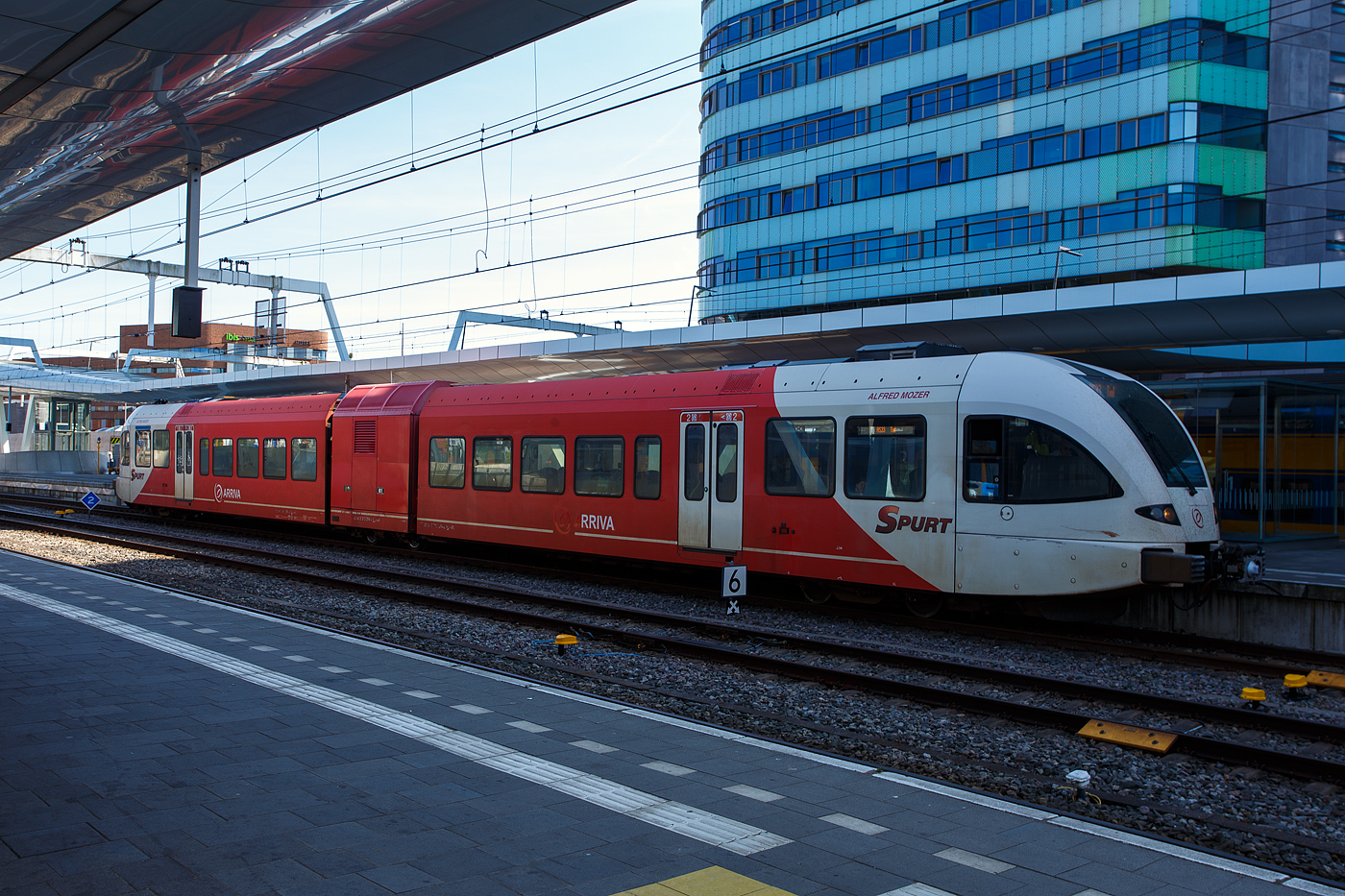 Der diesel-elektrische Stadler GTW 2/6 - Spurt 10.264 „Alfred Mozer“ der Arriva Nederland steht am 29 April 2025 im Bahnhof Arnhem Central (Arnheim Hbf), als Stoptrein RS33 nach Tiel, zur Abfahrt bereit. 

Der dieselelektrische Triebzug vom Typ Stadler GTW 2/6 der 4. Generation wurde 2012 von Stadler Rail im Werk Bussnang (Schweiz) gebaut.

GTW ist eine Leichtbau-Fahrzeugfamilie, die sich nicht nur äußerlich in unterschiedlichen Stirnfronten von eckig bis stromlinienförmig (wie hier bei der 4. Generation) unterscheidet und in verschiedenen Zusammenstellungen und Antriebsvarianten lieferbar ist, sondern auch in verschiedenen Spurweiten sowie als Zahnradbahnfahrzeug, wobei die Normalspurversionen UIC-konforme Vollbahnfahrzeuge sind. Das Grundkonzept des GTW ist eher unkonventionell: Ein mittiges Antriebsmodul, auch Antriebscontainer genannt, sorgt mit seinen beiden angetriebenen Achsen für den Antrieb des Triebzugs. Zwei leicht gebaute Endmodule mit je einem Drehgestell und Niederflureinstieg stützen sich auf das Antriebsmodul ab, was ein günstiges Traktionsgewicht bewirkt.

Das Konzept der GTW ergibt eine sehr gute Raumausnutzung der Endmodule. Außer über den Drehgestellen und an den aufgestützten Enden sind die GTW niederflurig ausgeführt (über 65 % Niederfluranteil). Durch Einfügen eines Mittelwagens, ebenfalls mit nur einem Drehgestell, kann ein GTW 2/6 zum GTW 2/8 ausgebaut werden. Statt des Mittelwagens kann aber auch ein weiteres Antriebsmodul eingefügt werden. Beim GTW 4/8 wurde zwischen den zwei benachbarten Modulen ein laufwerkloses Mittelteil eingehängt. Wenn zwei GTW 2/6 miteinander verbunden werden und zwei Führerstände wegfallen, entsteht ein GTW 4/12. Für betriebliche Flexibilität können bis zu vier GTW gleicher Bauart gekuppelt und über die Vielfachsteuerung gemeinsam gesteuert oder ein antriebsloser, einem Endwagen ähnelnder Steuerwagen mit der Achsformel 2’2’ mitgeführt werden.

Fahrzeuge der Arriva Nederland:
Die Arriva Nederland besitzt 96 GTW 2/6 bzw. 2/8 die zwischen 2006 und 2016 von Stadler in Bussnang (Schweiz), als diesel-elektrische bzw. elektrische (DC) Fahrzeuge gebaut, wurden. Bei den ab 2012 gebauten diesel-elektrischen GTW wurde zur Vergrößerung der Beinfreiheit die Raumaufteilung im Niederflurbereich angepasst. Grundsätzlich entsprechen die Fahrzeuge den bereits seit 2006 an Arriva gelieferten Fahrzeugen. Sie verfügen jedoch über einen neu entwickelten Antrieb mit Deutz- statt MAN-Motoren.

2005 bestellte Arriva für die Bedienung der niederländischen Provinzen Friesland und Groningen 22 Diesel-GTW 2/6 und 29 Diesel-GTW 2/8, davon sind 8 für den Einsatz nach Deutschland ausgerüstet. Die Züge mussten in nur 29 Monaten gebaut und geliefert werden. Weil damals in den Niederlanden die verschärften Crashnormen bereits in Kraft waren, mussten die Endwagenkästen mit Führerkabine neu entwickelt werden. Zusätzlich zur Druckfestigkeit von 1.500 kN wurde der Wagenkasten auf eine Versagenslast von 3.000 kN und das Energieabsorptionsvermögen bei einer Kollision von rund 900 kJ auf 2100 kJ erhöht. Die Frontstruktur und die Seitenwände der Wagenkästen wurden mit den Flirt-Wagenkästen vereinheitlicht, wobei seither eine integrale, komplette geschweißte Bauweise mit Aluminium-Strangpressprofilen zur Anwendung kommt. Damit wird eine höhere Stabilität der Rohbaustruktur erreicht. Zur Vereinfachung der Zulassungen sind die meisten sicherheitsrelevanten Funktionen in Relais-Technik realisiert.

2007/08 erhielt auch Veolia Transport Niederlande zwei- und dreiteilige Diesel-GTW, die weitgehend denen von Arriva entsprechen. Nach den Lieferungen der Diesel-GTW an Arriva und Veolia gewannen beide Unternehmen auch Ausschreibungen für mit 1.500 Volt Gleichspannung elektrifizierte Strecken. Die dafür gelieferten GTW sind mit Stromrichtern ausgestattet, die auf Basis der 3-kV-Flirt-Stromrichter entwickelt wurden. Die elektrischen und dieselbetriebenen Züge von Veolia verkehren in gemischter Mehrfachtraktion. Dazu sind alle Züge mit Schaltern sowohl für den Dieselmotorstart als auch für Hauptschalter und Stromabnehmer ausgestattet.
Antrieb mit Dieselmotoren (diesel-elektrisch):
Die GTW mit Dieselantrieb der ersten Generation wurden mit einem Zwölfzylinder-V-Motor des Typs 83-TD13 von MTU Friedrichshafen mit 550 kW Nennleistung ausgestattet. Wegen der Breite des Zwölfzylindermotors musste der Durchgang durch das Antriebsmodul asymmetrisch angeordnet werden. 

Bei der zweiten Generation wurden zwei schnelllaufende, wassergekühlte Sechszylinder-Lkw-Reihenmotoren mit je 390 kW Nennleistung von MAN eingebaut, die die strengen Euro-3-Abgasvorschriften im Straßenverkehr erfüllen. Die Beschaffung von in großen Mengen produzierten Lkw-Motoren ist zudem kostengünstiger als von speziellen Dieselmotoren für Schienenfahrzeuge. Die beiden nun völlig getrennten Antriebsaggregate bieten eine größere Leistung als der MTU-Motor und den Vorteil der Redundanz, so dass bei Störungen mit einem Aggregat weitergefahren werden kann. Die beiden Dieselmotoren sind auf beiden Seiten des Antriebmoduls angeordnet und erlauben einen symmetrischen Durchgang von einem Fahrgastraum zum anderen.

Die 2012 für Arriva Gelderland beschafften Fahrzeuge (wie diese hier) erhielten je zwei neuentwickelte Deutz-Dieselmotoren vom TCD 16.0 V8. Der wassergekühlter 8-Zylinder Motor in V-Ausführung (90°) mit Common Rail Einspritzsystem, Turboaufladung und Ladeluftkühlung mit einer Leistung von 520 kW erfüllt die Abgasnormen EU Stufe V / US Tier 4. Bei einer Drehzahl von 1.400 U/min erbringt der Motor ein maximales Drehmoment von 2.890 Nm.
Weitere Motordaten:
Hubraum: 15.9 l (Bohrung Ø 123 mm x 140 mm Hub)
Leistung: 520 kW (697 PS) bei 2.100 U/min
Max. Drehmoment: 2.890 Nm bei 1.400 U/min
Leerlaufdrehzahl: min. 600 U/min
Länge x Breite x Höhe: 1.150 x 945 x 1.170 mm
Gewicht (trocken): 1.260 kg

Die redundante Antriebsausrüstung besteht aus 2 Antriebssträngen mit je 1 Dieselmotor, Asynchrongenerator, IGBT-Stromrichter und Asynchronfahrmotor

TECHNISHE DATEN der GTW 2/6:
Spurweite: 1.435 mm (Normalspur)
Antriebsart: dieselelektrisch
Achsfolge: 2'Bo'2'
Inbetriebsetzung: 2006-2016
Länge über Kupplung 40.890 mm
Fahrzeugbreite 2.950 mm
Fahrzeughöhe 4.035 mm
Fußbodenhöhe: Niederflur 830mm / Hochflur 996 mm
Türen je Seite: 2 je 1.300 mm breit
Dienstgewicht (tara): ca. 68 t
Achsabstand im Drehgestell: 2.100 mm
Triebraddurchmesser: 860 mm (neu)
Laufraddurchmesser: 750 mm (neu)
Max. Leistung am Rad: 600 kW 
Anfahrzugkraft: 80 kN
Höchstgeschwindigkeit: 140 km/h
Sitzplätze in der 2. Kl.:  92 (Sommer Layout) /100 (Winter Layout)
Sitzplätze in der 1. Kl.:  8
Klappsitze: 18 (Sommer Layout) / 11 (Winter Layout)
Sommer Layout bedeutet das mehr Platz für Fahrräder vorhanden ist.

Abweichende TECHNISHE DATEN der GTW 2/8:
Achsfolge: 2’2’Bo’2’
Länge über Kupplung 55.937 mm
Türen je Seite: 3 je 1.300 mm breit
Dienstgewicht (tara): ca. 87 t
Sitzplätze in der 2. Kl.: 148 (Sommer Layout) /156 (Winter Layout)
Sitzplätze in der 1. Kl. 16
Klappsitze: 21 (Sommer Layout) / 14 (Winter Layout)