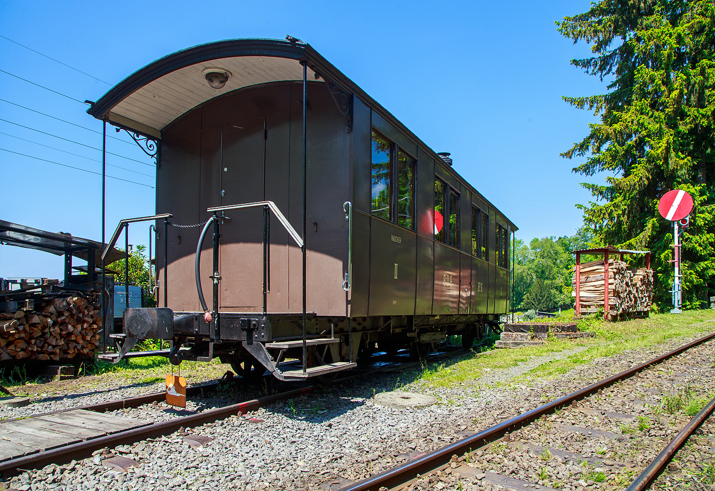 Der dreiachsige 2.Klasse Personenwagen BOB B� 6 „Kaiserwagen“ ehemals der Berner Oberland-Bahn (BOB), seit Dezember 2013 bei der Museumsbahn Blonay–Chamby (BC), hier steht er am 27.05.2023 bei der Dampflok-Wartungsstelle beim Museumsareal in Chaulin.

Die finanziellen Verh�ltnisse der Berner Oberland-Bahn waren schon alleine des Saisonbetriebes wegen nie so richtig gut. Der Personenwagenbestand war lange Zeit f�r die Tage mit hohem Verkehrsaufkommen eher unterdotiert. Die Eisenbahngesellschaft bem�hte sich wiederholt mit kleineren Einzelbestellungen den Personenwagenbestand aufzustocken.1900 wurden aus diesem Grunde bei der damaligen Schweizerischen Waggonfabrik (SIG) vier dreiachsige Personenwagen bestellt. Es waren dies der B� 5, B� 6, C� 25 und C� 26, die alle in gr�ner Farbe 1901 abgeliefert wurden, wobei die beiden C� gleich gebaut waren. Die beiden B� unterschieden sich jedoch voneinander.

Der Wagen wurde 1901 von Schweizerische Industrie Gesellschaft (SIG) in Neuhausen am Rheinfall (damals noch als Schweizerische Waggonfabrik gef�hrt) gebaut. F�r den Wagen B� 6 wurden 13.500 Franken bezahlt. Der Wagen ist ein Einzelst�ck, als er 1901 in Dienst gestellt wurde, war dieser Wagen der komfortabelste der BOB. Seine Innenausstattung aus bequemen Polsterb�nken, war der 1. Klasse anderer Bahnen w�rdig.

Der B3 6 wurde frisch revidiert f�r den geplanten Besuch des deutschen Kaisers Wilhelm II im Herbst 1912 im Berner Oberland bereitgehalten. Der Kaiser benutzte aber den Wagen mit seinem Gefolge f�r einen Besuch im Berner Oberland nicht, da er l�nger als geplant am Kaiserman�ver des III. Armeekorps der Schweizer Armee in der Ostschweiz verweilte. Zu diesem Zeitpunkt erhielt der Personenwagen den Spitznamen „Kaiserwagen“. Mit nur 24 Sitzpl�tzen bleibt der Wagen die meiste Zeit als Reserve und wird nur an Tagen mit starkem Verkehr genutzt.

1956 wurde der Wagen ausrangiert und 1959 an die Meiringen-Innertkirchen-Bahn (MIB) verkauft. Diese baute ihn vom B� zum B� (Zweiachser) um und setzte den Personenwagen, nun als B� 2 nummeriert, jahrelang im Sch�lerverkehr ein. Bei diesem Umbau wurden die 24 Sitze der Polsterklasse durch 32 Sitze der Holzklasse ausgetauscht. Da dies im Zeitraum des Wechsels von drei Wagenklassen auf zwei Wagenklassen erfolgte, wurde der Wagen immer als B (2. Klasse) bezeichnet.

Im Jahr 1978 kehrte der Personenwagen von den Modelleisenbahnfreunden Eiger Zweil�tschinen (MEFEZ) gekauft zur�ck auf das meterspurige Bahnstreckennetz der Berner Oberland-Bahnen. Dort wurde er wieder vom B� zum B� umgebaut und mit einer Bareinrichtung versehen. Der blau-wei�e Anstrich wurde durch einen historisch braunen Anstrich mit passender zeitgen�ssischer Beschriftung ersetzt. Ab 1980 konnte der Personenwagen als Barwagen mit weiterhin 16 Sitzen der Holzklasse in den historischen Z�gen und f�r Extrafahrten eingesetzt werden. Diesbez�glich hatte er die Zulassung f�r eine maximale Geschwindigkeit von 75 km/h f�r BOB Netz, sowie SBB Br�nigbahn (Interlaken–Luzern). Da Sonderz�ge auf einem stark befahrenen Streckennetz immer schwieriger zu organisieren sind, wurde der Wagen 2013 an die Museumsbahn Blonay-Chamby verkauft.

TECHNISCHE DATEN:
Baujahr: 1901
Hersteller: SIG, Neuhausen am Rheinfall
Spurweite: 1.000 mm (Meterspur)
Achsanzahl: 3 (bei MIB 2)
L�nge �ber Puffer: 9.980 mm
Breite: 2.600 mm
L�nge Wagenkasten: 10.000 mm (mit Plattformen)
Drehzapfenabstand: 5.600 mm
Achsabstand: 2 x 3.100 = 6.200mm
Eigengewicht: 8,6 t
H�chstgeschwindigkeit: 75 km/h
Sitzpl�tze:16
Quellen: Museumsbahn BC, x-rail.ch und wikipedia
