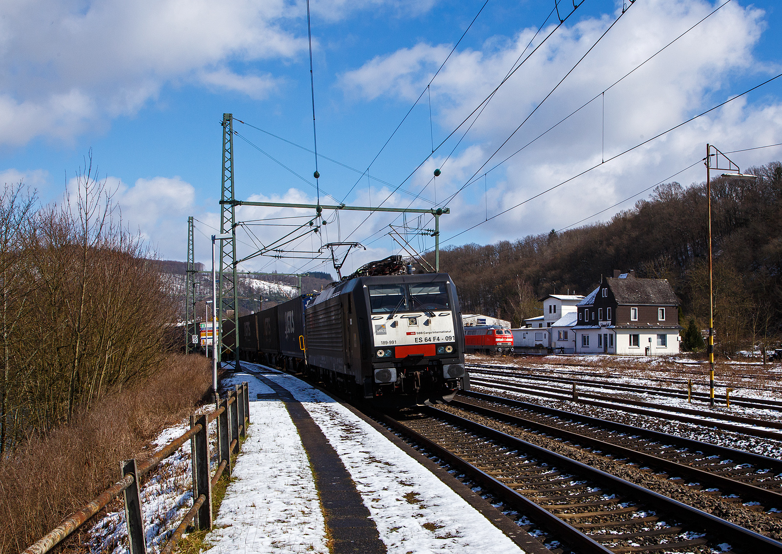 Die an die SBB Cargo International AG vermietete MRCE Dispolok ES 64 F4 - 091 bzw. 189-991 / LZB 189 991-3 (91 80 6189 991-3 D-DISPO, Class 189-VE) fährt am 15.03.2023, mit einem KLV-Zug auf der Siegstrecke (KBS 460) durch Scheuerfeld (Sieg) in Richtung Köln. Während hinten beim Kleinbahnhof der WEBA (Westerwaldbahn) die 218 191-5 (92 80 1218 191-5 D-MZE) der MZE - Manuel Zimmermann Eisenbahndienstleistungen abgestellt ist.

Die SIEMENS EuroSprinter wurde 2004 von SIEMENS in München-Allach unter der Fabriknummer 20739 gebaut.

Die BR 189 (Siemens ES64F4) hat eine Vier-Stromsystem-Ausstattung. Sie ist in allen vier in Europa üblichen Bahnstromsystemen einsetzbar. Diese hier hat die Variante E und besitzt die Zugbeeinflussungssysteme LZB/PZB, ETCS, SCMT, ZUB, INTEGRA und ATB für den Einsatz in Deutschland, Österreich, Schweiz, Italien, Niederlande, Slowenien und Rumänien.

Die Stromabnehmerbestückung ist folgende:
Pos. 1: CH, FR (AC), LU (AC), BE (AC)
Pos. 2: IT, SI, HR (DC)
Pos. 3: NL (DC), CZ (DC), FR (DC), SK, LU (DC)
Pos. 4: DE, AT, NL (AC), DK, CZ (AC), HR (AC), HU, RO