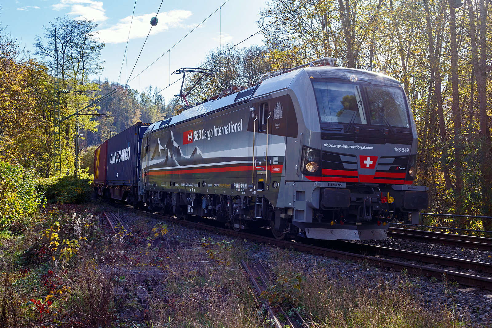 Ein fast fabrikneuer SIEMENS XLoad-Vectron, gerade mal 4 Wochen alt.
Die an die SBB Cargo International AG vermietete 193 539 mit XLoad  Duomo Milano  (91 80 6193 549-3 D-SIEAG) der SüdLeasing GmbH, Stuttgart (eingestellt in Deutschland durch Siemens) fährt am 29.10.2024 mit einem KLV-Zug, durch Kirchen (Sieg) in Richtung Siegen.

Die Multisystemlokomotive Siemens Vectron MS wurde 2024 von Siemens Mobilitiy in München-Allach unter der Fabriknummer 23595 gebaut und am 25.09.2024 ausgeliefert. Sie wurde in der Variante A40-1a ausgeführt und hat so die Zulassung für Deutschland, Österreich, die Schweiz, Italien, die Niederlande und Belgien (D / A / CH / I / NL / B). Sie verfügt über eine Leistung von 6,4 MW (160 km/h) und ist neben den nationalen Zugsicherungssystemen mit dem Europäischen Zugsicherungssystem (ETCS  BL3) ausgestattet. Zudem ist sie mit der neuen Ausrüstungspaket XLoad ausgestattet. 

Das neue XLoad Ausrüstungspaket für Vectron:
XLoad ist ein Ausrüstungspaket für Vectron, welches künftig mitbestellt, aber auch bei bereits ausgelieferten Vectron Loks nachgerüstet werden kann. Das Feature verbessert die Reibwertausnutzung und ermöglicht dadurch höhere Anhängelasten. Zudem reduzieren die Fahreigenschaften, die das Feature bewirken, den Verschleiß von Rad und Schiene.

Aktuell sind die Schweizer Vectron-Lokomotiven (SBB Cargo und BLS Cargo) in der Regel in Doppeltraktion unterwegs. Die Steigungen und Rampen der Schweizer Berge sind vor allem bei schlechten Witterungsbedingungen nicht ohne. Eine Lokomotive muss auch bei geringerem Schlupf genügend Traktion auf die Schienen bringen, um alle Güter sicher und zuverlässig ans Ziel zu bringen. Ein effizienter Weg aus dieser «Misere» ist die für Vectron entwickelte Zusatz-Funktion «XLoad». Den erfolgreichen Beweis trat eine SIEMENS Testlokomotive im Frühjahr 2022 bei der SBB Cargo International und bei der BLS Cargo eindrücklich an. 

Für SBB Cargo International bewies die Test-Lokomotive am Bözberg und für BLS Cargo an der Nordrampe des Lötschbergs ihre enorme Zugkraft. 
Vectron meisterte im Frühjahr 2022 die lange 12‰-Steigung des Bözbergs mit einer Anhängerlast von 2.000 Tonnen bravourös. Bei den nächtlichen Testfahrten zeigte sich eindrücklich die enorme Zugkraft der Lokomotive. 

Am Lötschberg wurden bei der BLS Cargo steigungsmäßig noch ein paar Promille draufgepackt. Mit 1.020 Tonnen im Gepäck bewältigte die Vectron-Lokomotive mit XLoad-Feature die 27‰-Steigung der Nordrampe ebenfalls meisterlich. Und auch diverse Anfahrtsversuche absolvierte der mit dem XLoad-Feature aufgerüstete Vectron problemlos. 

So bestellte die SüdLeasing GmbH (Stuttgart) im Auftrag der SBB Cargo International jüngst 20 Vectron Lokomotiven mit XLoad bei SIEMENS.