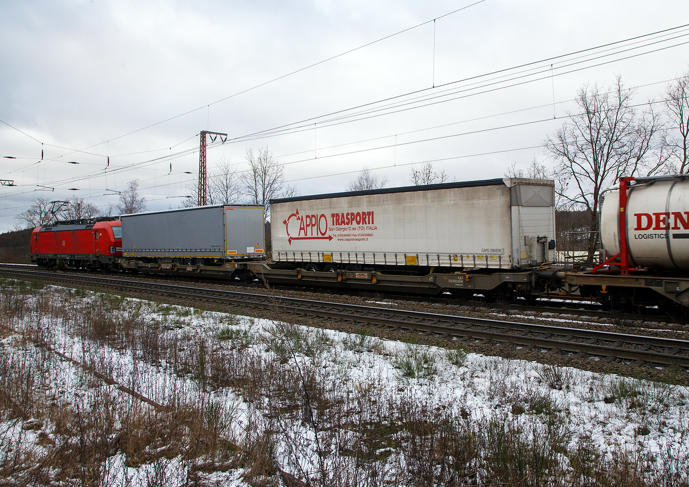 Hinter der DB 193 323-3....
Der sechsachsige Gelenk-Taschenwagen (Doppeltaschenwagen in Gelenkbauart), 33 85 4956 771-1 CH-HUPAC der Gattung Sdggmrss, der HUPAC Intermodal SA, am 27.01.2023 im Zugverband bei der Durchfahrt in Rudersdorf (Kr. Siegen), im Zugverband bei der Durchfahrt in Rudersdorf (Kr. Siegen), hier beladen mit zwei Sattelanhängern.

Diese Wagen vom Typ T5/T3000e wurde von Tatravagónka a.s. in Poprad (Slowakei) ab 2015 gebaut, die Entwicklung und auch Lizenzgeber ist die Ferriere Cattaneo SA in Giubiasco (Schweiz). Baugleiche Wagen sind auch bei anderen Halteren im Einsatz, die jeweils die Gattungskennzahl 4956 haben. Mögliche Ladeeinheiten sind zwei kranmanipulierbare Sattelauflieger oder alternativ bis zu vier Wechselbrücken und/oder Container. Dafür besitzt der Wagen einen dreifach verstellbaren Stützbock sowie für die Ladungseinheiten feste und klappbare Aufsetzzapfen auf den Langträgern. Das maximale Zuladegewicht beträgt für Sattelauflieger 2 × 40 t; die Basishöhe liegt bei 270 mm über SO.

TECHNISCHE DATEN:
Spurweite: 1.435 mm
Länge über Puffer: 34.200 mm
Drehzapfenabstand: 2 x 14.200 mm
Achsabstand in den Drehgestellen: 1.800 mm
Laufraddurchmesser: 920 mm (neu) / 860 mm (abgenutzt)
Ladelänge: 2 × 16.185 mm
Eigengewicht: 36.200 kg
Max. Zuladung bei Lastgrenze S: 98,8 t (ab Streckenklasse D)
Max. Zuladung bei Lastgrenze SS: 83,8 t (ab Streckenklasse C)
Max. Geschwindigkeit: 100 km/h / bei Lastgrenze SS und leer 120 km/h
Kleinster  befahrbarer Kurvenradius: R 75 m (R 150 m im Zugverband)
Intern. Verwendungsfähigkeit: TEN – GE

Die Bedeutung der Gattungs- und Kennbuchstaben (hier  Sdggmrss):
S - Drehgestell-Flachwagen in Sonderbauart
d - für den Transport von Straßenfahrzeugen eingerichtet
gg - für den Transport von Containern über 60 Fuß eingerichtet
m - bei mit sechs o. mehr  Radsätzen Ladelänge 18 m bis unter 22 m
r - Gelenkwagen
ss - Höchstgeschwindigkeit (beladen) bis zu 120 km/h