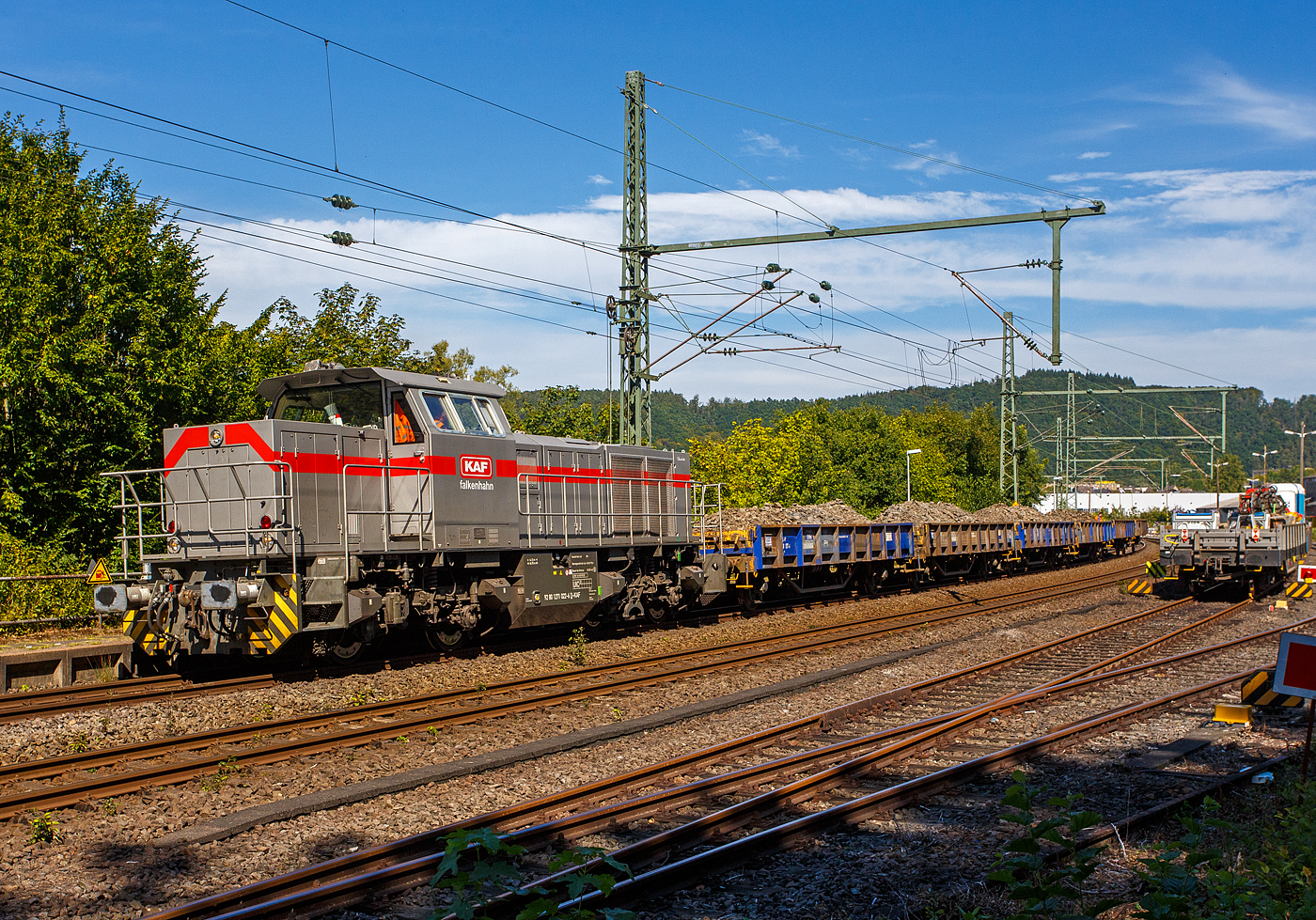Nun drückt die 271 022-6 „Charlotte“ (92 80 1271 022-6 D-KAF) eine Vossloh/MaK G 1000 BB der KAF Falkenhahn Bau AG. ex MRCE bzw. ex HGK DH 49, am 26 August 2025 den mit Aushub beladenen Niederbordwagen-Zug (zweiachsiger Flachwagen NS Gattung Klmos 702 der Vermietungsfirma Railpro), von der Baustelle im Bf Scheuerfeld/Sieg ca. 3 km nach Betzdorf/Sieg. Beim Rbf Betzdorf befindet sich die Umladestation, hier wird der Aushub von Baggern abgeladen und zwischengelagert. 

Vom 22 August bis 12 September 2025 ist die Siegstrecke zwischen Troisdorf und Siegen für drei Wochen voll gesperrt. Grund ist die Umleiter-Ertüchtigung der Siegstrecke. Hier im Bereich Bahnhof Scheuerfeld/Sieg ist eine der viele örtlichen Baustellen.

Die Generalsanierung folgt ab Dezember 2026: Diese dreiwöchige Sperrung der Siegstrecke ist ein Vorgeschmack auf das kommende Jahr. Ab Dezember 2026 und bis Juli 2027 soll die Siegstrecke erneut voll gesperrt werden. Dann möchte die Bahn den Abschnitt umfassend modernisieren, kilometerweise Gleise, Schwellen und Schotter tauschen.
