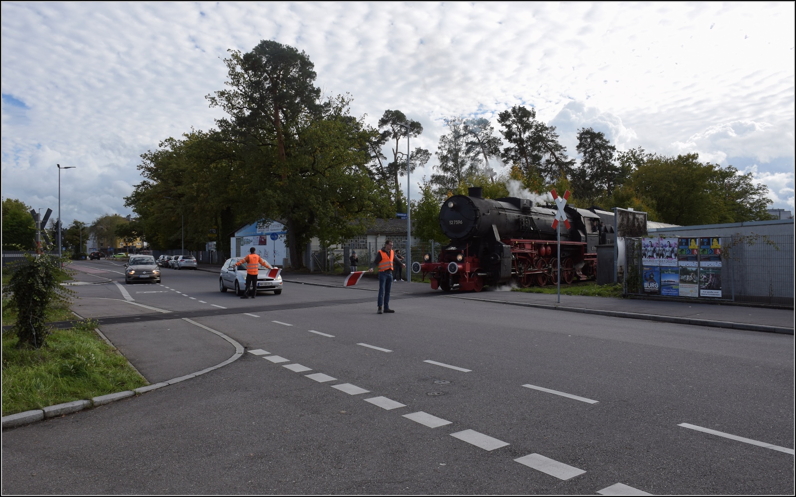 Schienenverkehr unterm Hohentwiel. 

52 7596 mit ihrem EFZ-Sonderzug für die SEHR & RS auf der nächsten Station bei der Bahnübergangsralley in Singen in der Bohlinger Strasse. Ein Autofahrer lässt sich das hautnahe Spektakel, pardon blechnahe Spektakel nicht entgehen. Oktober 2022.