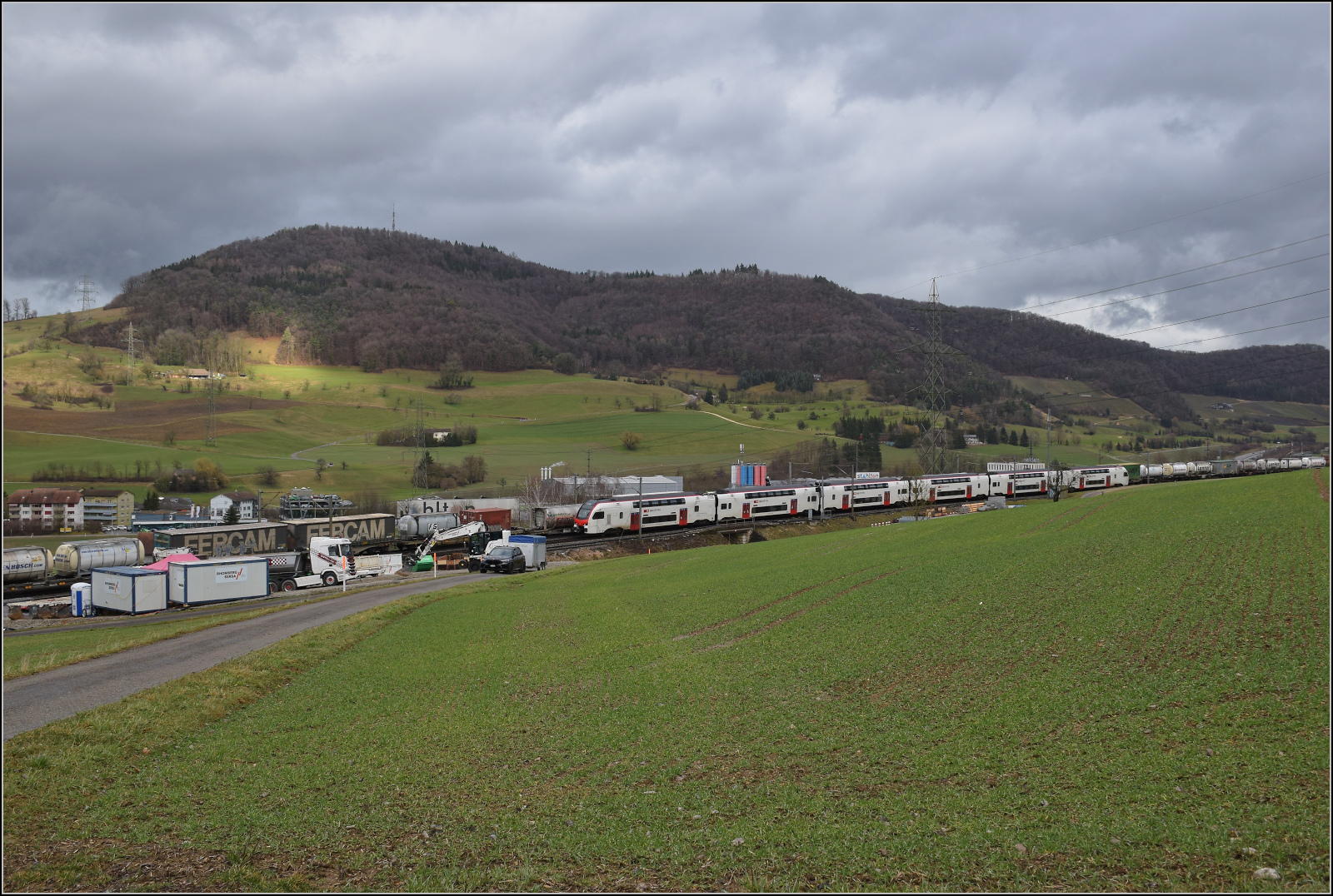 Schlechtwetter und ein Baustellendrama bei Frick. 

W�hrend nun RABe 512 034 auf dem Weg nach Basel sich just vor der Baustelle mit dem G�terzug von 193 549 'Duomo Milano' kreuzt, wird die Absicht der Probleml�sung auf der Baustelle deutlich. Ein Gleisbagger soll beim Rausziehen des LKW aus den selbstgegrabenen L�chern helfen. Februar 2026.