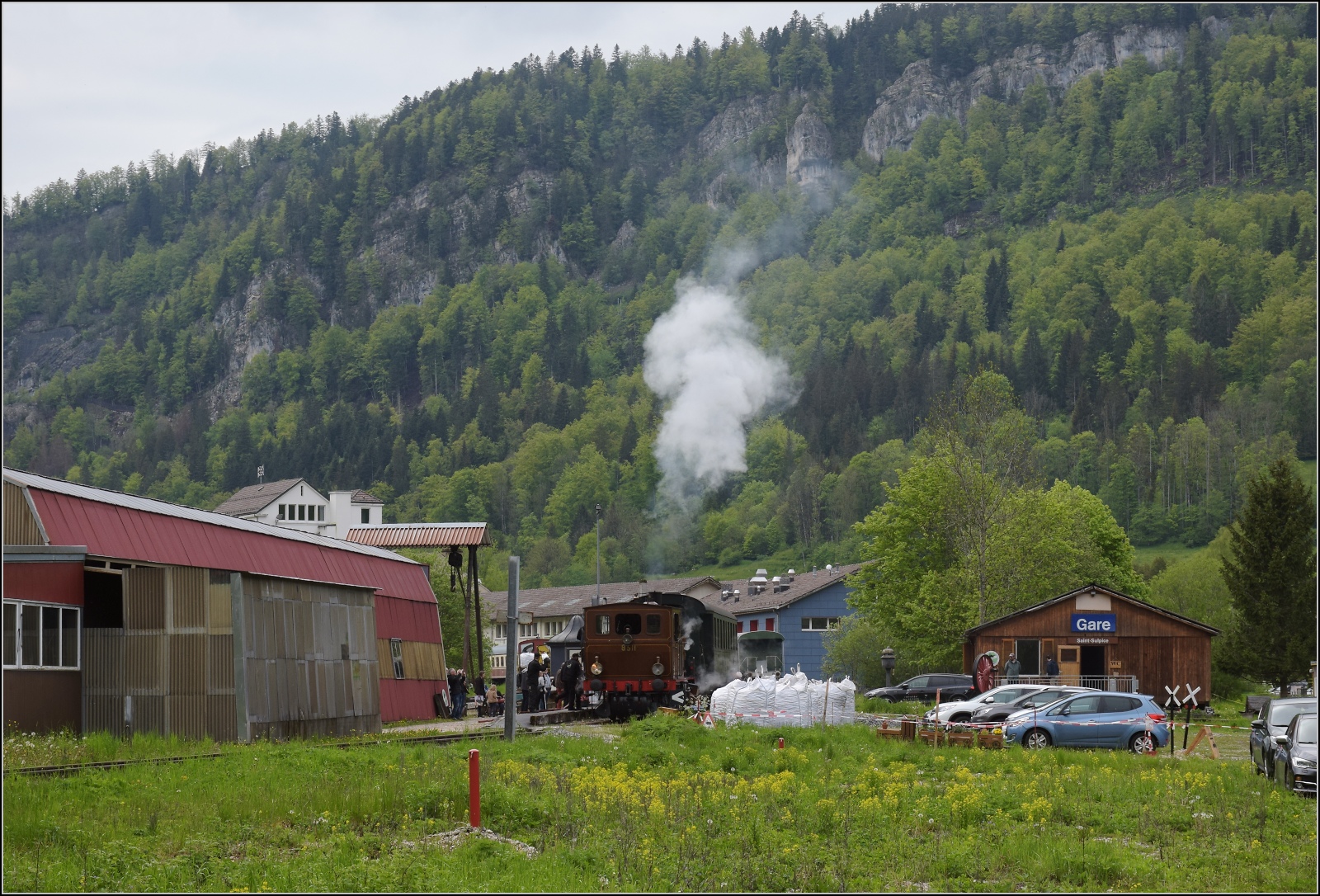 Vapeur Val-de-Travers: Train du Terroir.

Bereitstellung des Zuges von und mit E 3/3 8511 in St-Sulpice. 

Die etwas unmotivierte Motivauswahl gilt es allerdings zu erklären. Wer genau ins Bild schaut, erkennt etwas links der Dampfwolke unterhalb der Unterbrechung der Felswand zwei Masten und ganz links im Bild auch noch mal. Die Hauptstrecke nach Frankreich via dem zuvor gezeigten Bahnhof Les Verrières geht durch diese Felswand ins noch einmal 200 m höher gelegene Hochtal zur Wasserscheide. St-Sulpice an der Karstquelle der Areuse und später Buttes mussten daher regional erschlossen werden. Das wurde seinerzeit durch die RVT gemacht, die heute in die TransN integriert ist. Das schaffte immerhin dieses kleine Biotop für die Dampfenthusiasten des VVT. Dazu Mai 2023. 